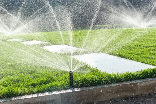 Irrigation sprinklers running across a lawn and paver walkway